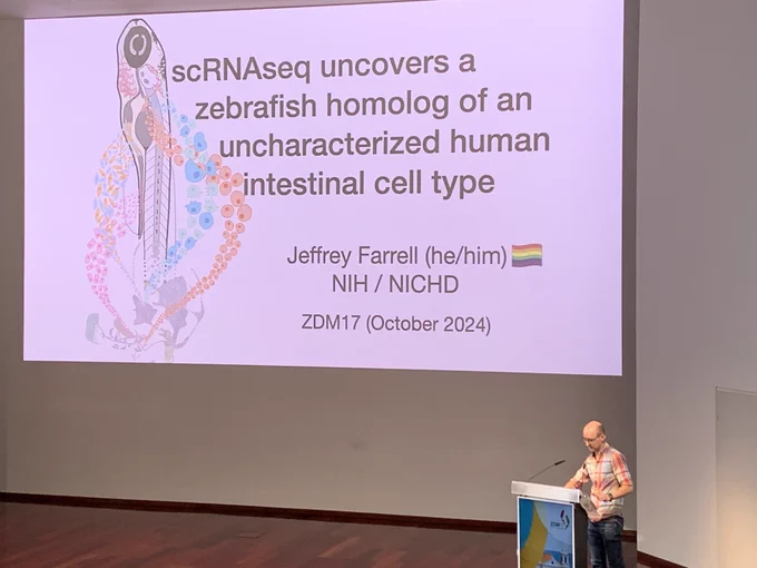 Dr. Jeffery Farrell standing on a stage next to a podium with a large screen with his talk titled, “scRNAseq uncovers a zebrafish homology of an uncharacterized cell type”