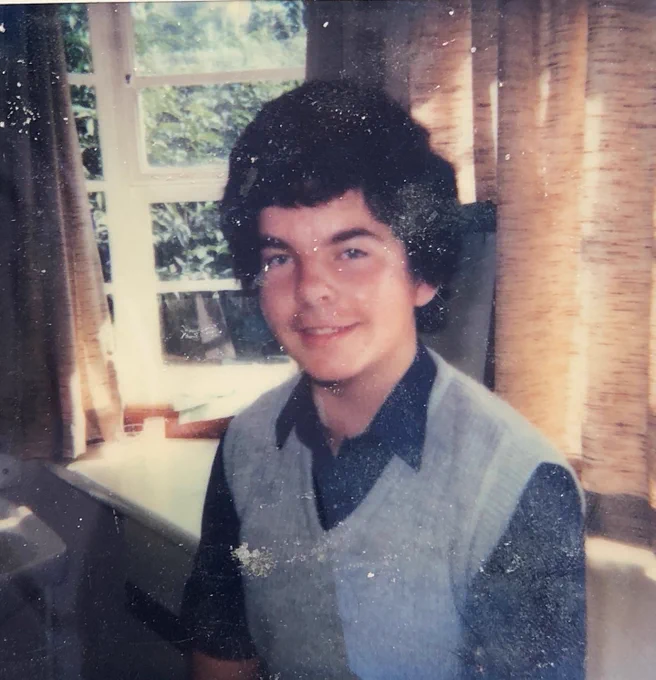 Photo of Clive after his transplant at Harefield Hospital. He is wearing a dark shirt and grey vest, and is stood in front of a window.