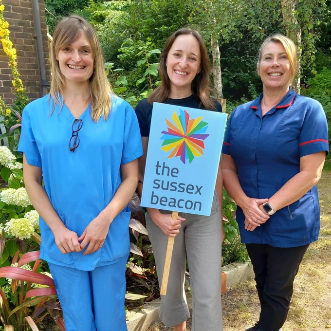 Some members of The Sussex Beacon Impatient Unit team, including doctors and nurses. They are holding a sign that has the Sussex Beacon logo