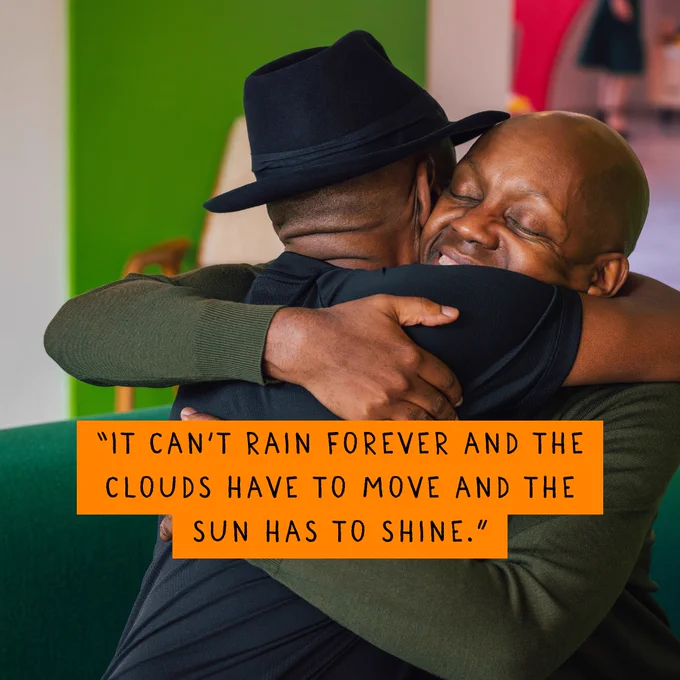 Two men hugging. Quote on image says: 'It can't rain forever and the clouds have to move and the sun has to shine'.