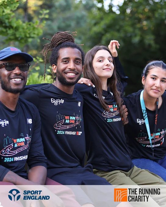 Four individuals wearing '2024 Finisher' T-shirts from The Running Charity, seated outdoors with trees in the background, smiling and looking relaxed.