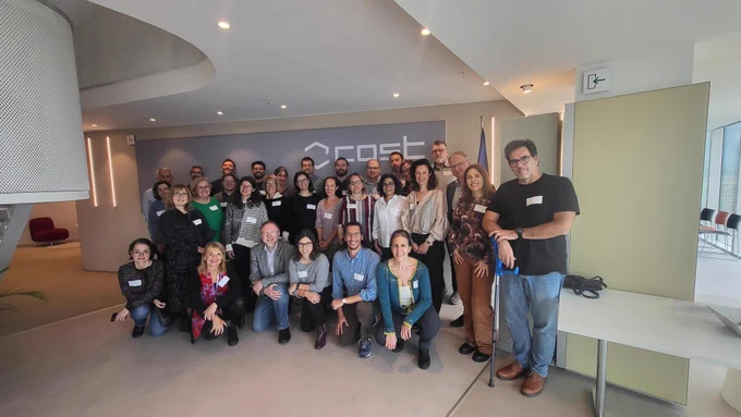 A group of 30 researchers in the COST Office, a mix of men and women of different ages, attending the kick off meeting for their new research network. They are all standing close together posing for a photo.