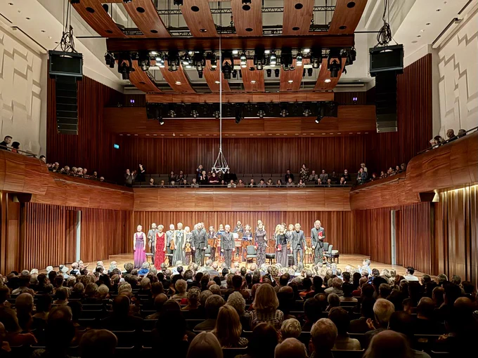 Performers on the stage at London's Milton Court Concert Hall receive applause from audience in the foreground.