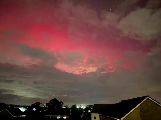 An image of the aurora with partly cloudy skies in East Devon. Houses are situated at the bottom of the image.