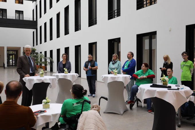 Foto aus dem Innenhof des Bundesministeriums für Arbeit und Soziales in Berlin. Staatssekretär Dr. Rolf Schmachtenberg begrüßt mehrere Personen aus den Behindertenwerkstätten zum Schichtwechsel. Mehrere Personen versammelten sich um einzelne Stehtische.