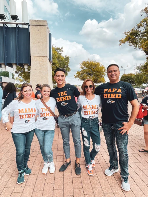 Five people wearing family-themed t-shirts ("Mama Bird," "The Bird," "Papa Bird") smiling outdoors at a sporting event, possibly at a stadium.