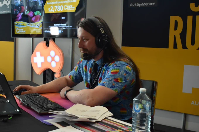 Sten at the host desk looking intently at the host computer with a light smirk. His hand graces the mouse.