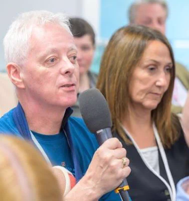 Left to right: Eamonn Dunne holding a microphone with Cathy Low sitting next to him.