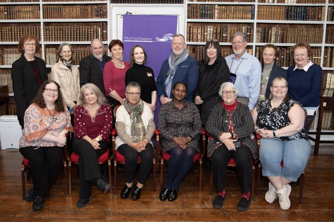 Group of sixteen people formally standing and seated in front of old bookcases.