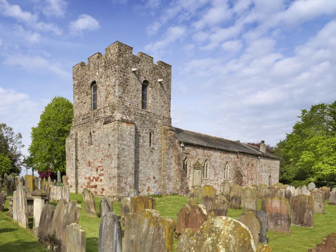 A photograph of a late 12th-century church with later alterations and additions built of sandstone, surrounded by gravestones.