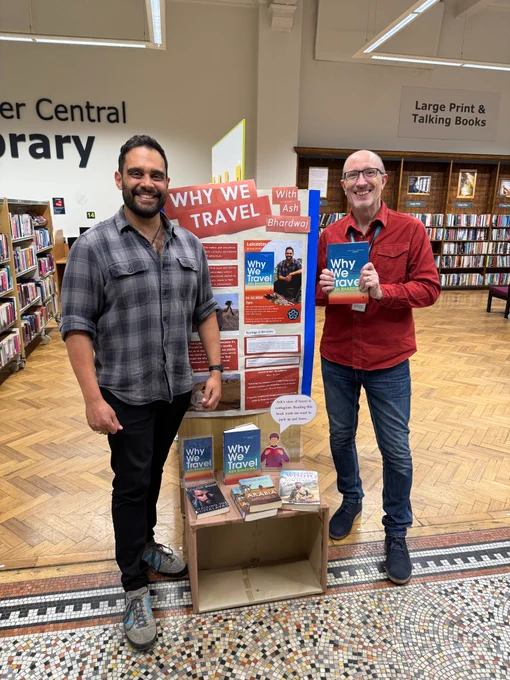 Author Ash Bhardwaj and a member of staff from Leicester Libraries stood in front of a display about Ash's book Why We Travel