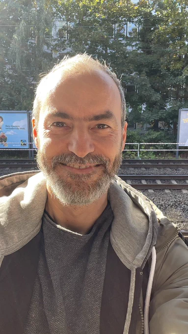 Torsten Landsiedel Selfie am Bahnhof. Im Hintergrund sind Gleise zu sehen. Ich lächle wegen Vorfreude.