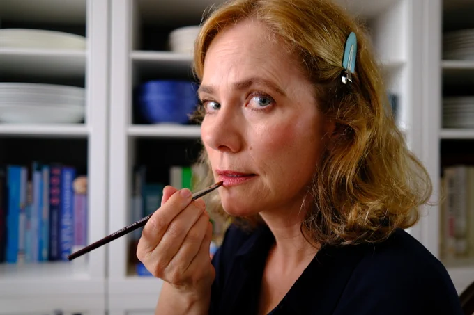 An older white woman is putting lipstick on
