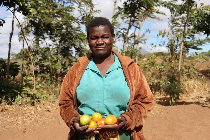 A head shot of Roseby Mukawa. She is holding crops in her hands.