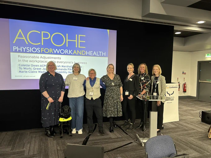 A group of presenters of the network session standing in front of a screen. There is a guide dog wearing harness sitting in the front.