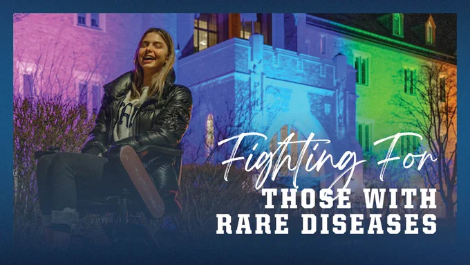 Junior student Annie Hamilton is outside the Jordan Hall of Science, illuminated in pink, blue and green, on Rare Disease Day, February 28, 2023. 