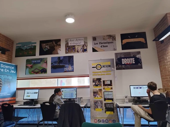 Une salle avec des posters de jeu et deux personnes devant des ordinateurs