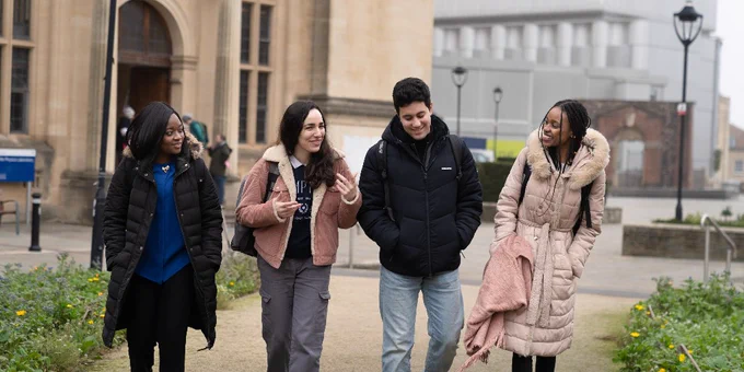 Four students are walking and chatting together on a university campus.