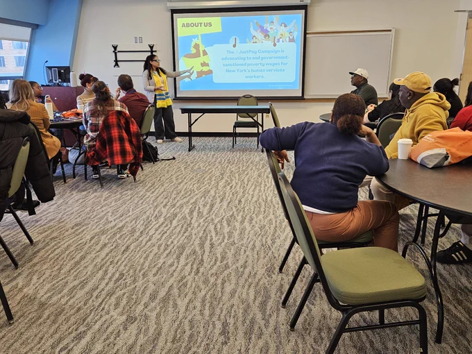 An HSC staff member in a yellow scarf stands in front of a slide reading "Urban Pathways Participation in JustPay"