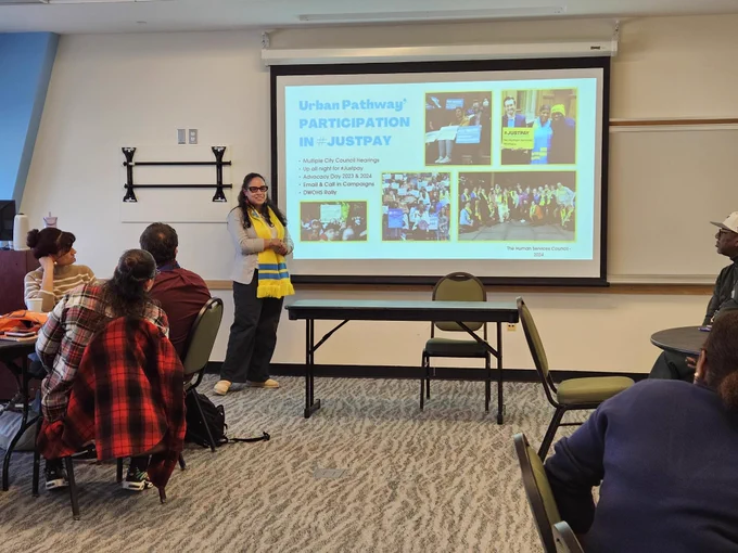 An HSC staff member in a yellow scarf stands in front of a slide reading "Urban Pathways Participation in JustPay"