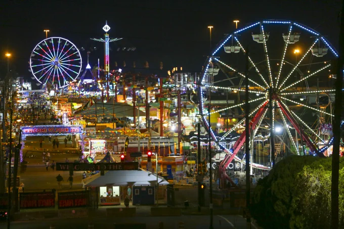 Nighttime view of the vibrant Mississippi State Fair with multiple Ferris wheels and colorful lights.