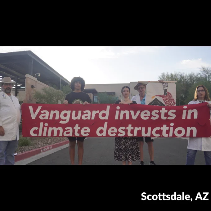 Five people hold banners, including a large red banner with white text. Photo by Joe Weeks.