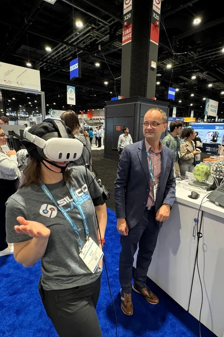 A SilicoLabs team member demos wears an fNIRS cap and VR headset, while another team member looks on at the Brain Products booth.