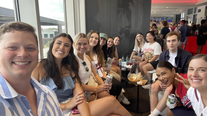Group of people enjoying a gathering at a sports venue, smiling and seated at a table with snacks and drinks.