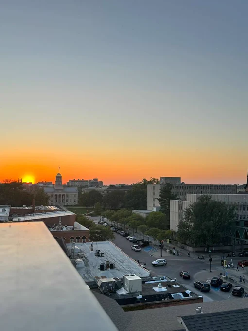 Photo of downtown Iowa City from a rooftop, as the sun sets behind the Old Capitol Building.