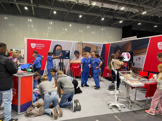 Attendees engage in interactive activities at a Middlesex University London exhibition booth at a science fair, featuring medical equipment and educational displays.