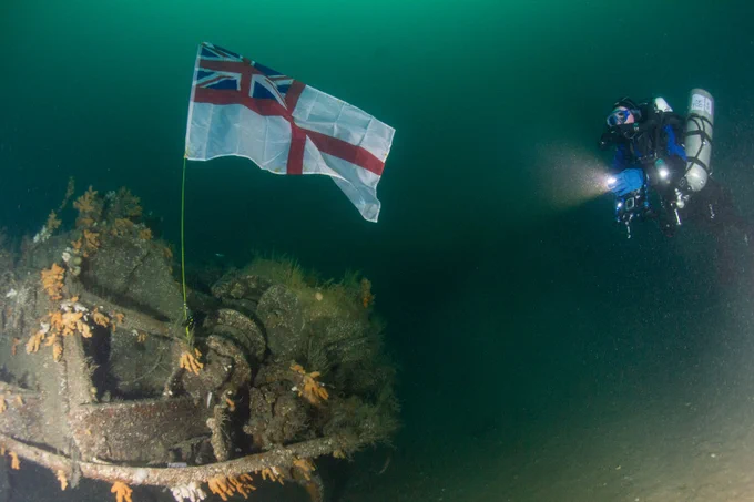 Lt Cdr Jen Smith shines her torch on the White Ensign over the wreck of HMS Exmouth