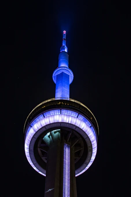 Closeup of the CN Tower at night lit blue and white / Gros plan de la Tour CN illuminée en bleu et blanc. 