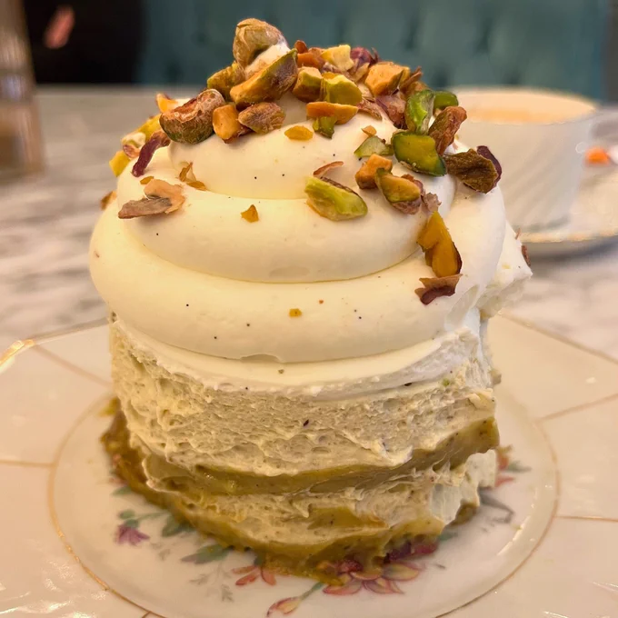 A cake made of pistachio biscuit base topped with piles of pistachio mousse and vanilla cream and pistachio nuts