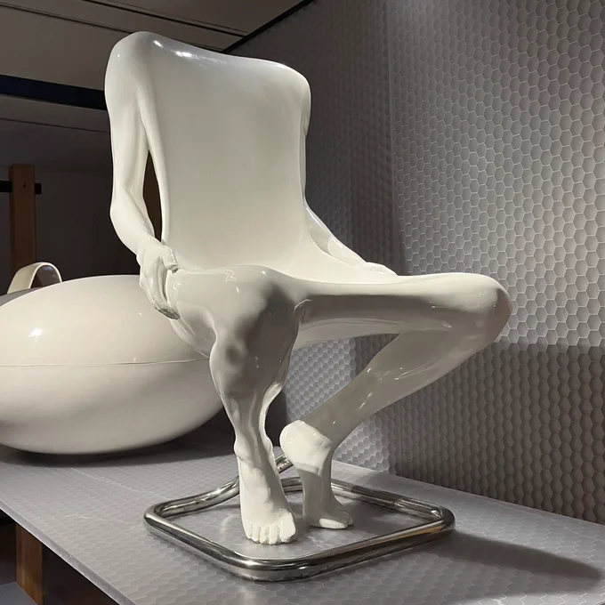 Front view of a chair designed in 1970 by Ruth Francken, currently on display at the Musée des Arts Décoratifs in Paris. It’s made of white polyurethane, and is shaped like a seated nude man with no head. The seat part is hollowed out of his chest and lap.