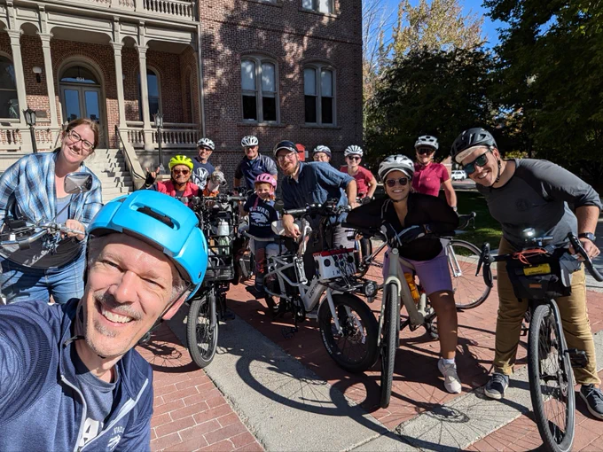 About 15 people and a dog pose on bikes in front of Morrill Hall