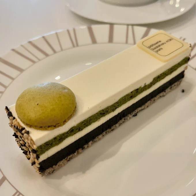 A slim rectangular slice of cake, made up of bands of sesame biscuit, matcha sponge and cognac cream. There’s a small green matcha macaron perched at one end.