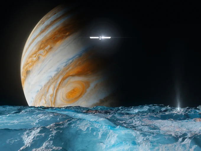 Illustration of Europa Clipper spacecraft flying above the surface of Jupiter's moon Europa. The large gas giant planet Jupiter, with swirls of color and the Great Red Spot seen, appears in the background. The spacecraft appears small and bright with solar arrays extended on each side. Europa's surface is frozen ice. Credit: NASA JPL