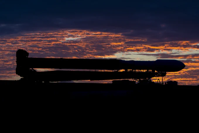 Silhouette of the horizontal SpaceX Falcon Heavy rocket being rolled out to the launchpad at sunset in preparation for the Europa Clipper launch from Kennedy Space Center.