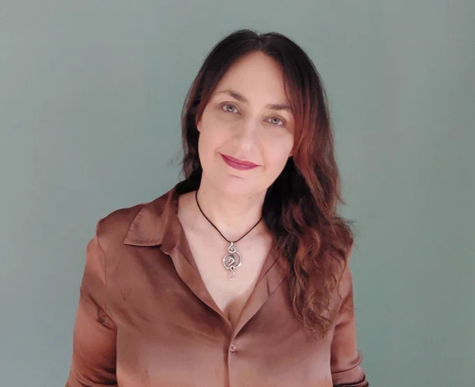 Dr Christine Padget, wearing a brown shirt in front of a plain background, smiling at the camera. 