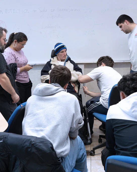 Grupo de personas rodeando a una persona en silla de ruedas mientras realizan mediciones o ajustes en uno de sus brazos.

