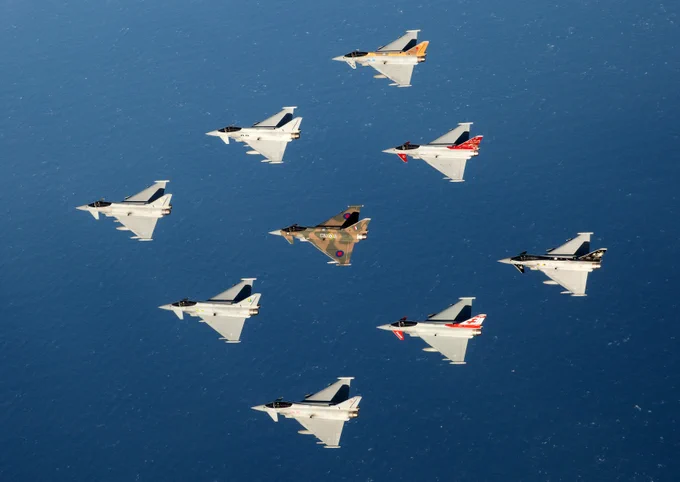 Image of nine RAF Typhoons, all painted in various squadron and display colours flying over the sea together in a diamond formation.