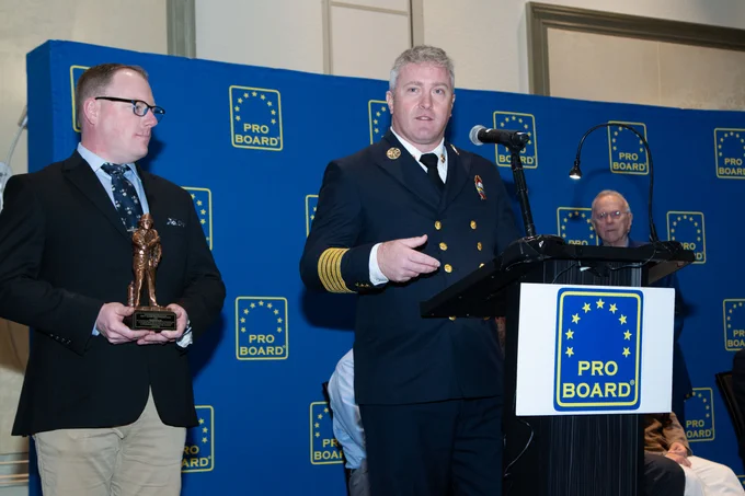 Director Mark Wholey gives an acceptance speech while Curriculum Administrator Max Dodge holds the award.