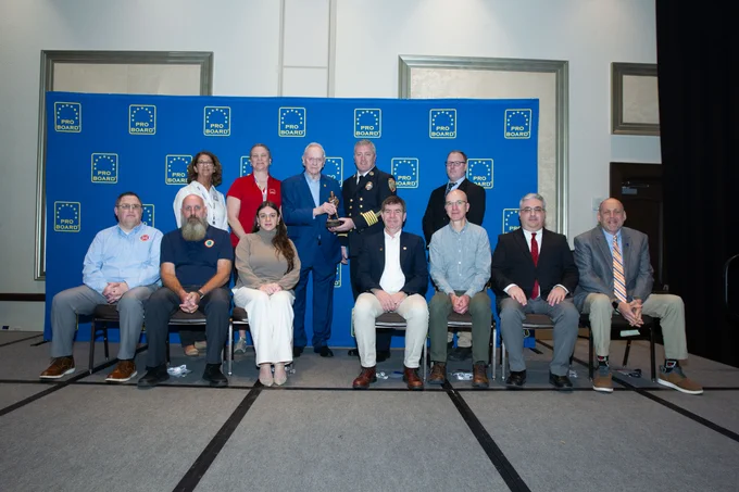 Group photo of Director Mark Wholey and Curriculum Administrator Max Dodge accepting the award from the Pro Board.