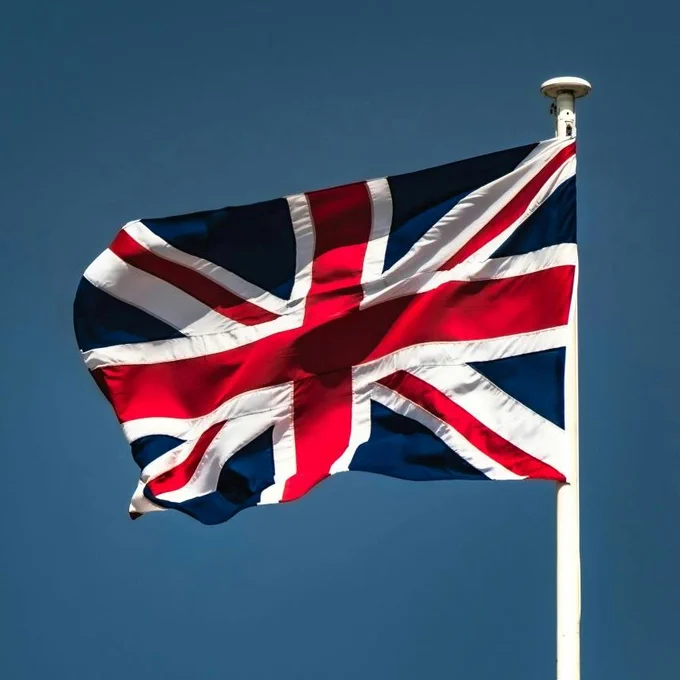 The flag of Great Britain on a flagpole fluttering in the wind against a dark blue sky.
