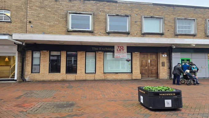 Terraced two storey brick building with pedestrian walkway in front.