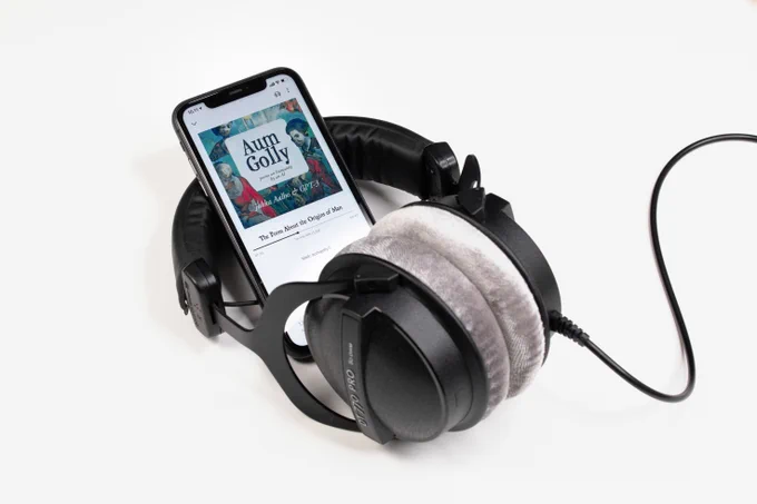 A smartphone displaying an audiobook cover is nestled in large black headphones with plush ear pads. 
