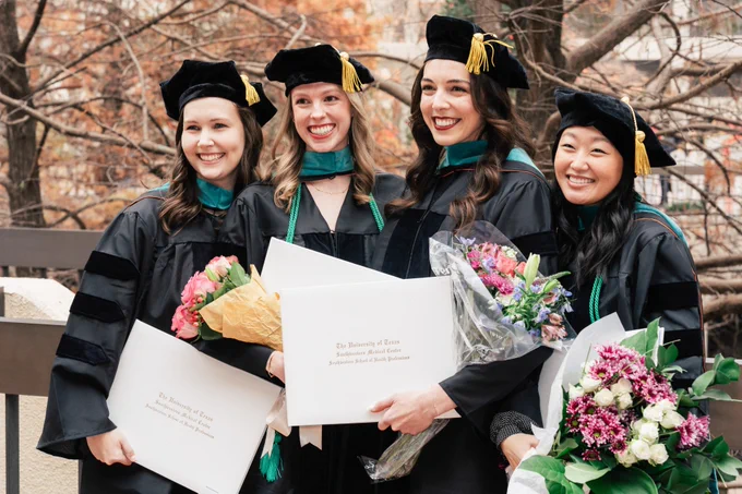 Four graduates in black caps and gowns, holding bouquets and diplomas from the University of Toronto, smiling joyfully.