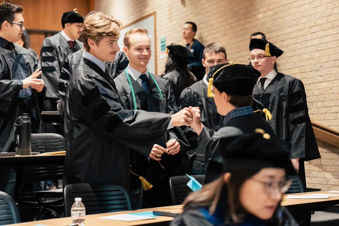 Students in graduation attire shaking hands and celebrating during a graduation ceremony.