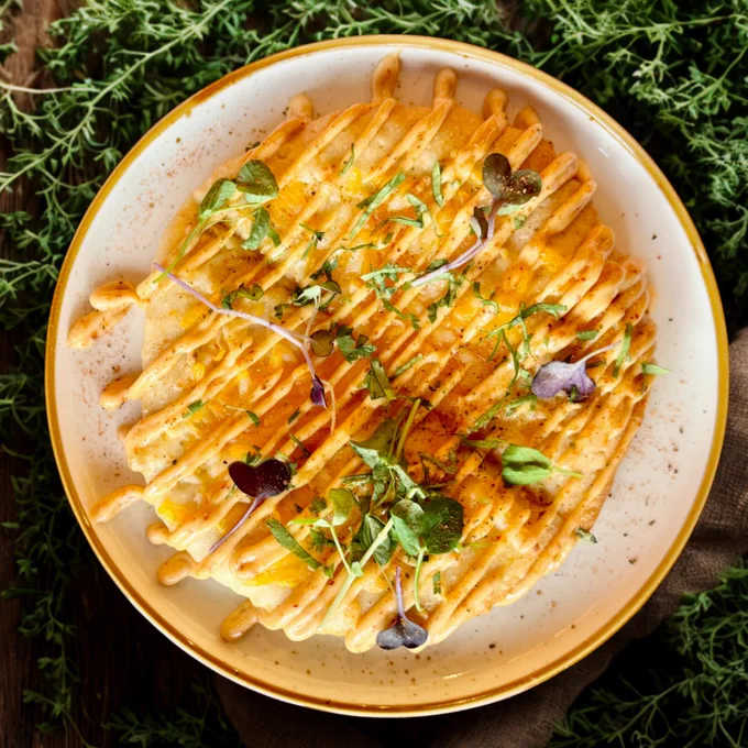 Plate of golden-brown enchiladas topped with creamy orange sauce and fresh green microgreens on a rustic wooden table.
