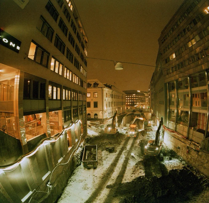 Snowy building site in between office buildings in downtown Oslo at night.